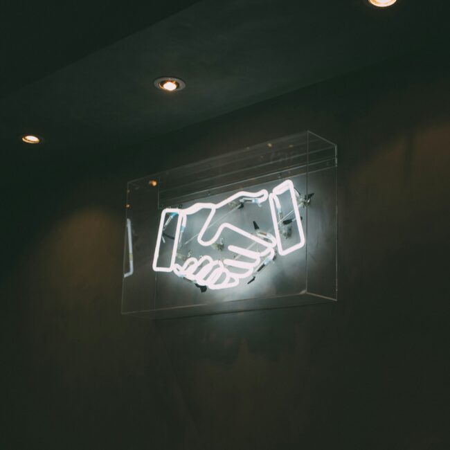 Neon sign with handshake in white on a black background