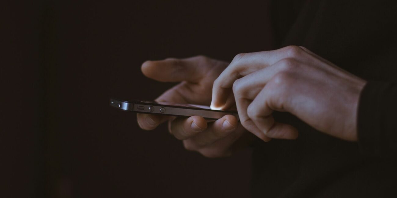 Two hands on a black background, scrolling on a smartphone