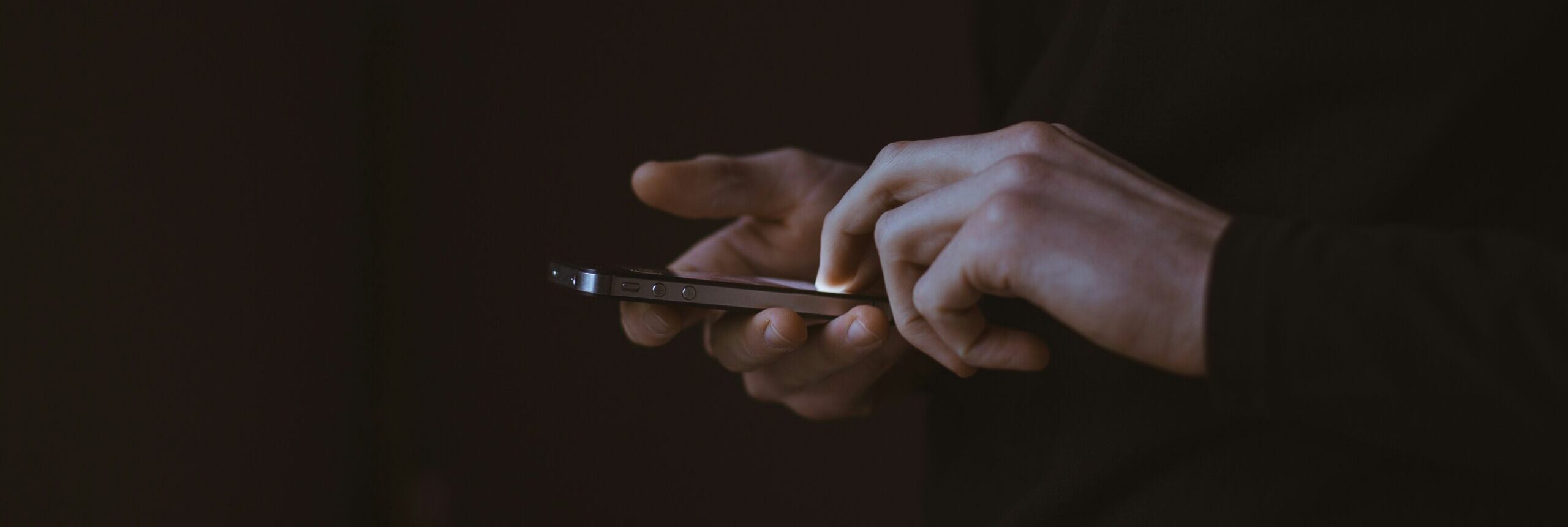 Two hands on a black background, scrolling on a smartphone