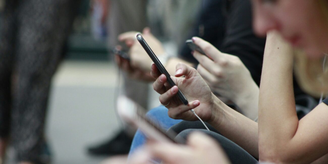 Hands of teenagers sitting next to each other and all on their cell phones