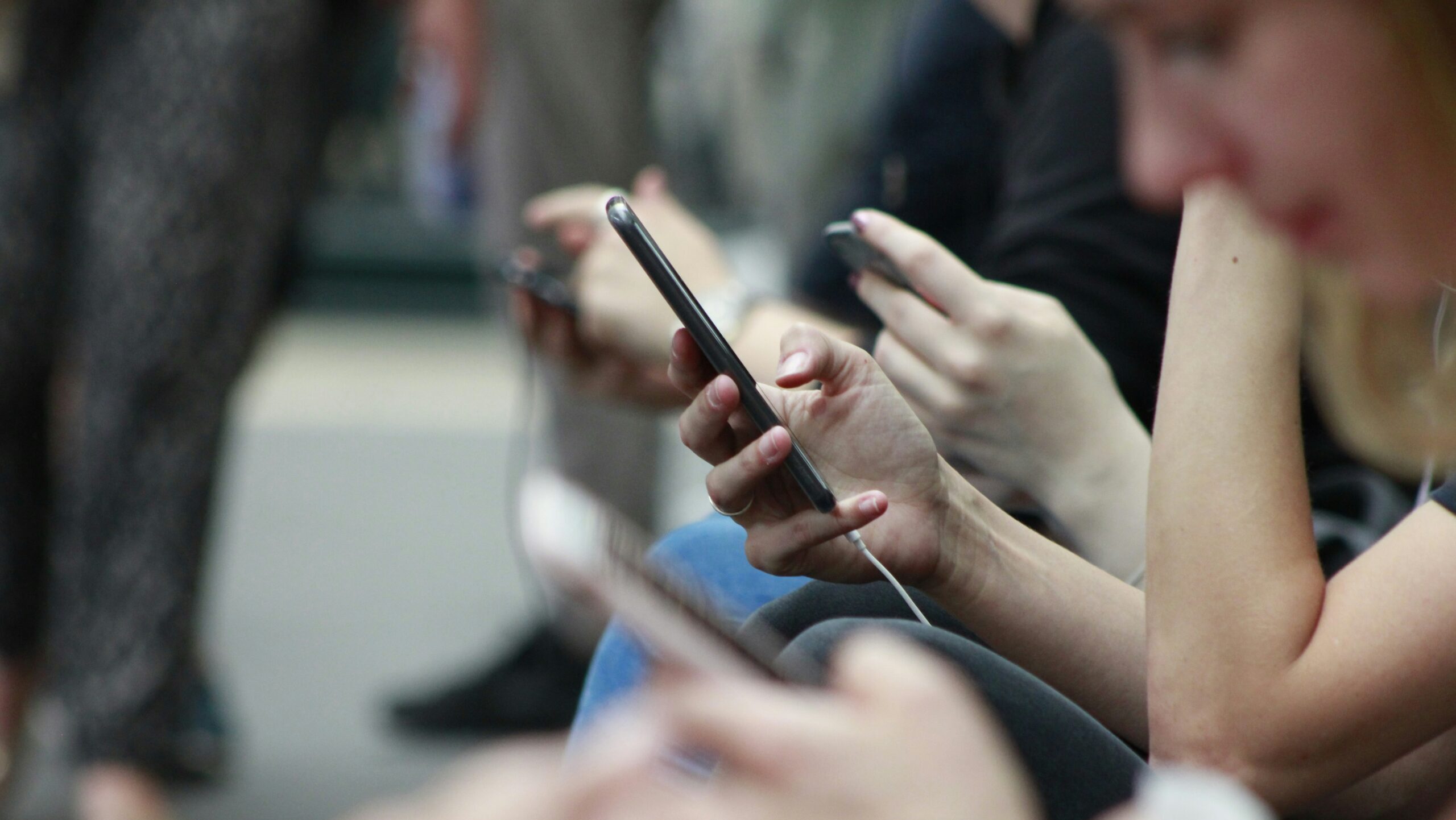 Hands of teenagers sitting next to each other and all on their cell phones